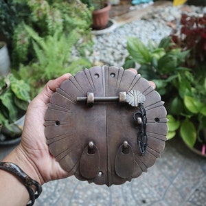 Puede incluir: Un pestillo de puerta de latón vintage con un diseño floral decorativo. El pestillo tiene una cadena y un pequeño ojo de cerradura.