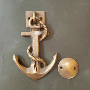May include: Brass door knocker shaped like an anchor with a rope design. The knocker is mounted on a square plate and has a round, brass base.