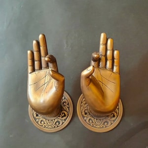 May include: Two ornate brass door handles shaped like hands in a prayer position. The handles are mounted on decorative plates with intricate floral designs.