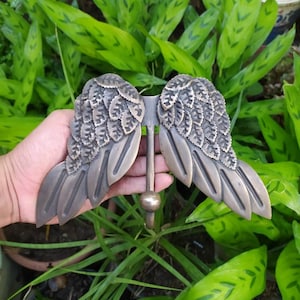May include: A brass angel wing hook with a detailed design of overlapping leaves. The hook is a decorative and functional piece for hanging items.