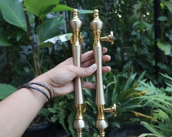 May include: A pair of gold door handles with a decorative design. The handles are held in a hand with a bracelet.