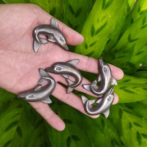 Könnte beinhalten: Fünf kleine silberne Delfin-Figuren, jede in einer anderen Pose, werden auf einer Hand präsentiert. Die Delfine sind aus Metall und haben eine glatte, polierte Oberfläche.