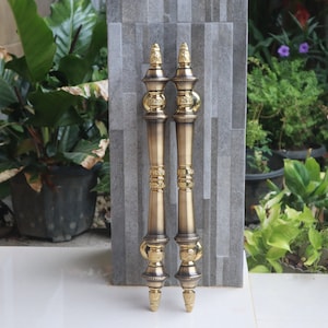 May include: A pair of ornate gold door handles with intricate details and a pointed finial. The handles are made of metal and have a polished finish.