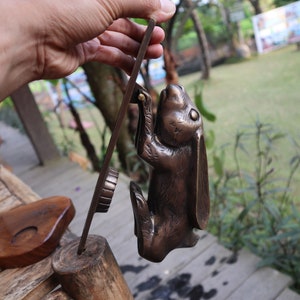 May include: A bronze rabbit door knocker with a detailed design. The rabbit is standing on its hind legs with its front paws raised. The knocker is attached to a wooden base.