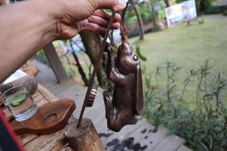 May include: A bronze rabbit door knocker with a detailed design. The rabbit is standing on its hind legs with its front paws raised. The knocker is attached to a wooden base.