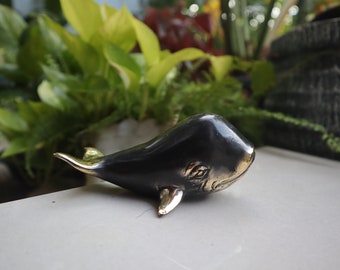 May include: A small, black and gold whale figurine. The whale is made of metal and has a shiny finish.
