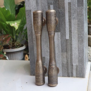 Könnte beinhalten: Zwei verzierte Messing-Türgriffe mit komplizierten geometrischen Mustern. Die Griffe sind zylindrisch und haben eine dunkle, gealterte Oberfläche.