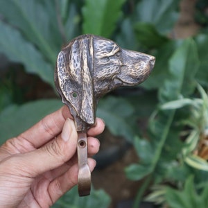 May include: A brass dog head coat hook with a detailed design. The hook is in the shape of a dog's head, with a realistic depiction of the dog's features. The hook is a great way to add a touch of rustic charm to any home.