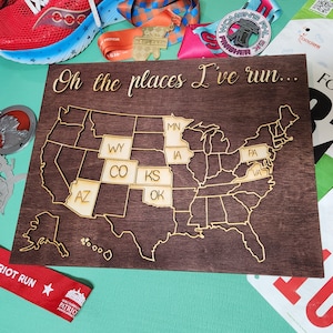May include: A wooden map of the United States with the text "Oh the places I've run..." at the top. The states of Arizona, Colorado, Kansas, Oklahoma, Wyoming, Minnesota, Iowa, Pennsylvania, and Virginia are highlighted in gold.