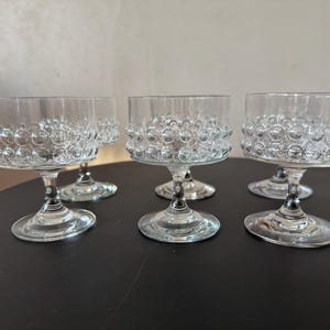 May include: Set of five clear glass stemmed cocktail glasses. Each glass features a round bowl with a textured, bubble-like design around the rim. The glasses are displayed on a dark surface.