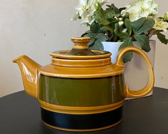 May include: A brown and green striped teapot with a black band around the bottom. The teapot has a lid and a handle.
