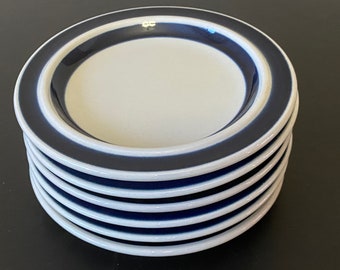 Könnte beinhalten: Ein Stapel von sechs weißen Keramiktellern mit blauem Rand. Die Teller haben ein schlichtes Design mit einem einzigen blauen Band am Rand.