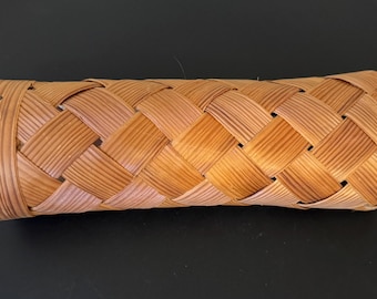 May include: A woven, rectangular basket with a rounded shape. The basket is made of light brown, interwoven strips of wood, creating a textured pattern. Small metal fasteners secure the ends. The basket is likely used for storage.