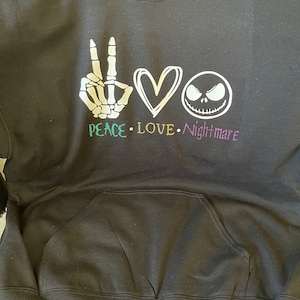 K&ouml;nnte beinhalten: Schwarzer Hoodie mit einem wei&szlig;en Peace-Zeichen, einem Herzen und einer Grafik von Jack Skellington. Der Text "Peace Love Nightmare" ist unter der Grafik gedruckt.