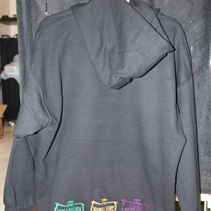 K&ouml;nnte beinhalten: Schwarzer Kapuzenpullover mit drei gestickten Patches am unteren Rand. Die Patches sind in Gr&uuml;n, Gold und Lila und zeigen den Text "Frog's Breath", "Work's Want" und "Death Don't Stop".