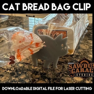 Puede incluir: Un clip para bolsa de pan con forma de gato gris que sujeta una bolsa de pan de plástico. El texto "CAT BREAD BAG CLIP" está en la parte superior. El texto inferior dice "DOWNLOADABLE DIGITAL FILE FOR LASER CUTTING". El logotipo de Sawdust Garage Studios está a la derecha.