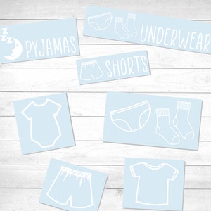 Puede incluir: Un conjunto de etiquetas azules con contornos blancos para organizar la ropa. Las etiquetas incluyen las palabras "Pijama", "Shorts", "Ropa interior" e imágenes de prendas de vestir como calcetines, ropa interior y camisas.