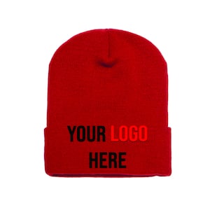 May include: A bright red beanie hat with the text "YOUR LOGO HERE" in black and red. The hat is made of a knitted material and is designed to be worn on the head. The text is centered on the folded brim.