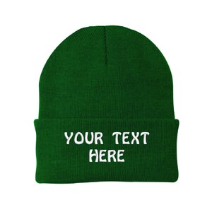 May include: A green knitted beanie with white embroidered text that reads "YOUR TEXT HERE".