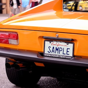 May include: A bright orange classic sports car with a white stripe down the back. The car has a California license plate that says "SAMPLE" and the text "Your Text Here" and "www.YOUR TEXT.com".