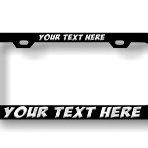May include: Black metal license plate frame with white text that says "YOUR TEXT HERE" on the top and bottom.