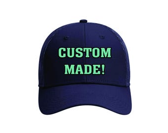 May include: Navy blue baseball cap with a mesh back and the words "CUSTOM MADE!" in bright green block letters across the front. The cap has a curved brim and a button on top.