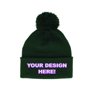 May include: A dark green beanie with a matching pom-pom on top. The folded cuff features the text "YOUR DESIGN HERE!" in white with a purple outline. This winter hat is a customizable accessory.