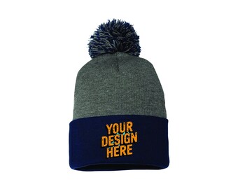 Può includere: Un berretto lavorato a maglia grigio con bordo blu navy e pompon blu navy. Il bordo presenta la scritta "YOUR DESIGN HERE" in arancione. Questo accessorio invernale è un berretto elegante.