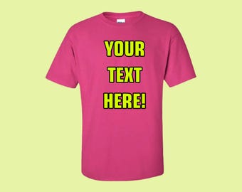 以下が含まれることがあります： 太字の黄色いフォントと黒いアウトラインで「YOUR TEXT HERE！」と書かれたマゼンタ色のTシャツ。 このシャツは半袖のクルーネックです。