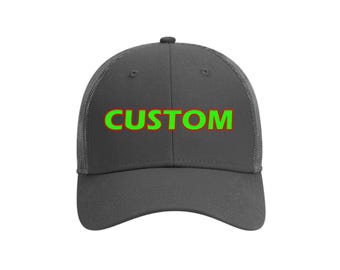 May include: A dark grey trucker cap featuring the word "CUSTOM" in green with a red outline. The cap has a curved peak and a mesh back. A practical and stylish accessory for various occasions.