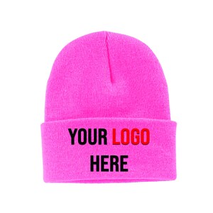 May include: A pink knitted beanie with the text "YOUR LOGO HERE" in black and red lettering.