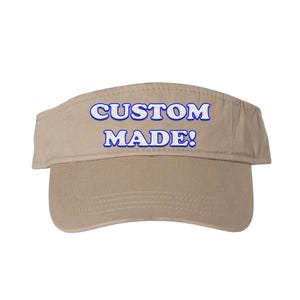 May include: A beige visor featuring the text "CUSTOM MADE!" embroidered in white with a blue outline. The visor is made of a sturdy fabric and has a curved peak to protect the eyes from sunlight.
