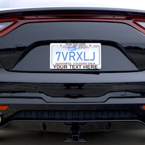 May include: Black car with a personalised number plate that reads "7VRXLJ" and the text "YOUR TEXT HERE" above and below the plate. The number plate also has the text "First to Flight" and "NORTH CAROLINA" on it.