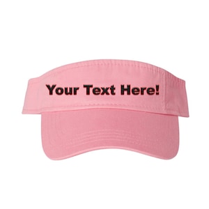Può includere: Visiera rosa chiaro con la scritta "Your Text Here!" in nero. La visiera ha una visiera curva e una fascia in tessuto. Questo accessorio è progettato per proteggere gli occhi dal sole.