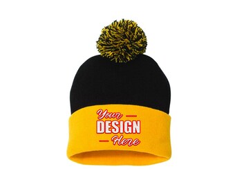 Può includere: Un berretto nero a maglia con bordo giallo e pompon giallo e nero. Il bordo giallo presenta il testo "Your DESIGN - Here" in rosso e bianco.