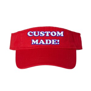 May include: A red visor with the text "CUSTOM MADE!" in white letters with a blue outline. The visor is a classic style, designed to shield the eyes from the sun.