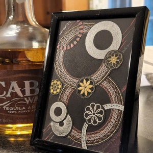 May include: A framed black and white abstract art piece with gold and red accents. The artwork features a series of concentric circles and geometric shapes.