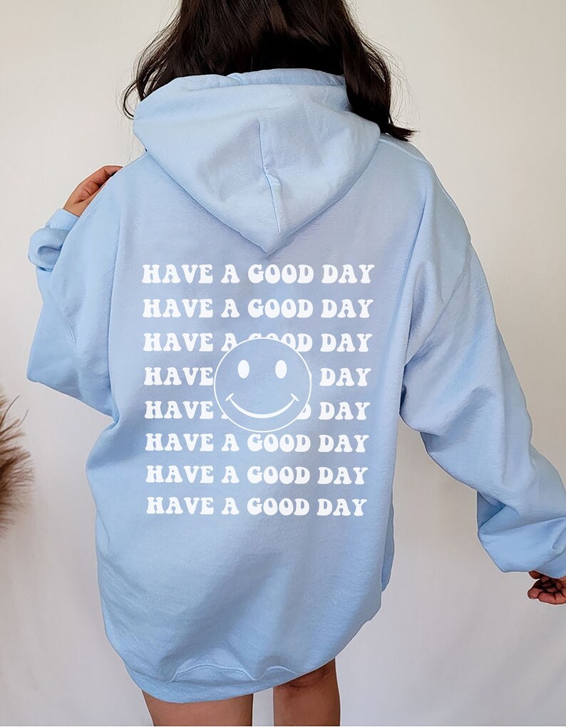 May include: Light blue hooded sweatshirt with the phrase "Have a good day" repeated multiple times in white text on the back. A smiley face is included in the text.