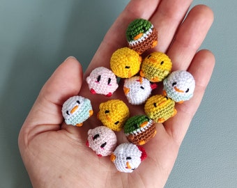 May include: A collection of small, crocheted chick ornaments in various colors, including yellow, white, pink, and green. Each chick has a detailed design with small beaks and eyes. The chicks are held in a hand against a teal background.