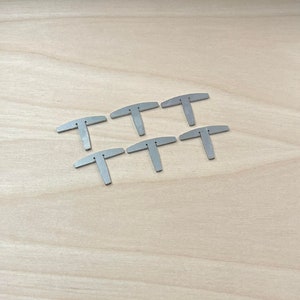 May include: Six silver metal T-shaped pieces on a light wood surface.