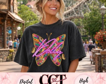 May include: A charcoal gray short-sleeve t-shirt featuring a large, colorful butterfly graphic on the front. The butterfly wings are filled with various patterns including leopard print and floral designs, overlaid with the neon pink script text Dolly.