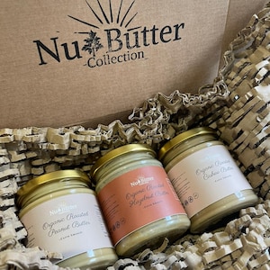 May include: Three glass jars of organic nut butter in a cardboard box. The jars are labeled "Organic Roasted Peanut Butter", "Organic Roasted Hazelnut Butter", and "Organic Roasted Cashew Butter".