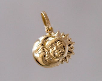 May include: A gold pendant charm featuring a sun and moon design. The sun has a face and the moon is crescent shaped.