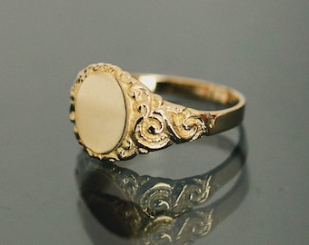 May include: A gold signet ring with an oval-shaped top and intricate scrollwork details.