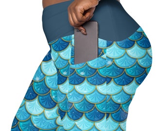 May include: Blue and teal leggings with a mermaid scale pattern. The leggings have a large pocket on the right side, with a black smartphone inside.