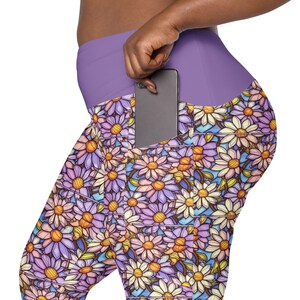 May include: Purple leggings with a floral print of colorful daisies. The leggings have a large pocket on the right side, with a black smartphone inside.