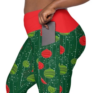 May include: Green leggings with a red waistband and a phone pocket. The leggings have a Christmas ornament pattern with red and green ornaments.