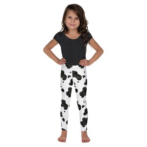 May include: A young girl wearing a black short-sleeved shirt and white leggings with a black cow print pattern.