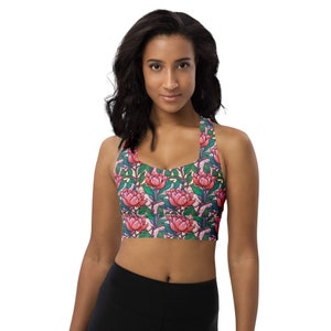 May include: A pink and green floral print sports bra with a racerback design. The bra has a wide elastic band and adjustable straps.