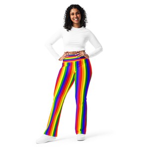 May include: A person wearing a white long-sleeved shirt and rainbow striped leggings. The leggings have a wide waistband and are made of a stretchy material.